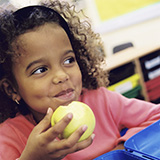 A young girl eats an apple in her classroom.