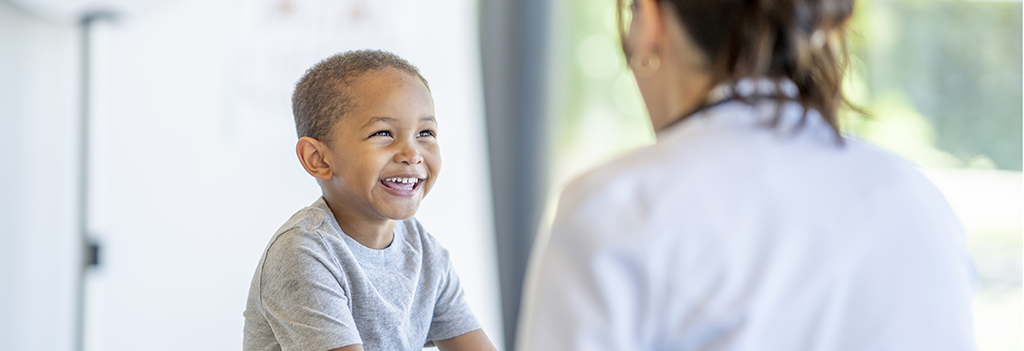 A young boy smiling and laughing while talking to a healthcare profesional