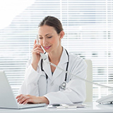 A doctor refers to a computer while on the telephone.