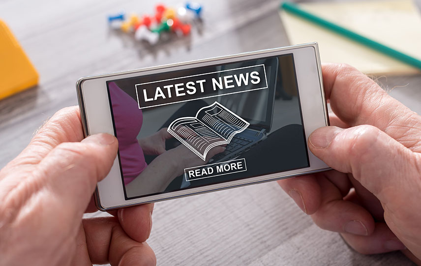 Hands holding a smartphone; screen reads Latest News Read More