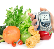 A hand holding a digital glucose monitor in front of a table full of fresh fruits and vegetables