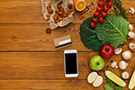 A mobile phone sits on a table near fruits and vegetables.