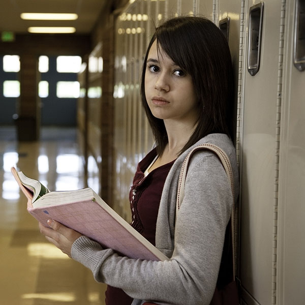 A teenage female leaning against a locker.